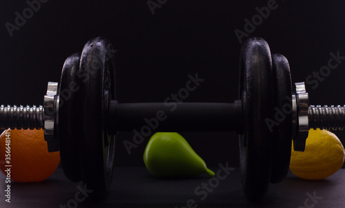 Black metal dumbbell for fitness with fruits, on a black background.