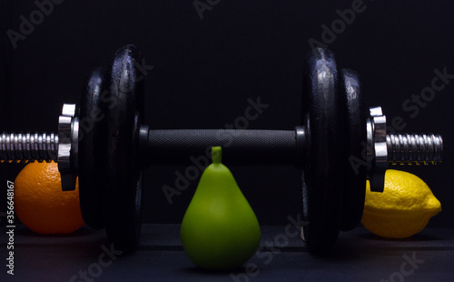 Black metal dumbbell for fitness with fruits, on a black background.