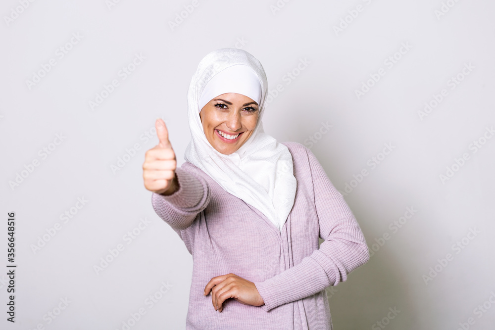 Smiling young middle eastern muslim woman looking at the camera with her thumbs up. Portrait of a beautiful muslim woman wearing hijab. Beautiful young Muslim woman wearing a hijab on her head