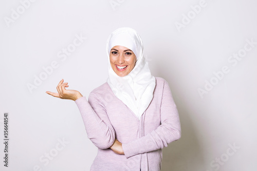 Modern, Stylish and Happy Muslim Woman Wearing a Headscarf. Arab saudi emirates woman covered with beige scarf. "Welcome" Face. One women smile with white background © Graphicroyalty