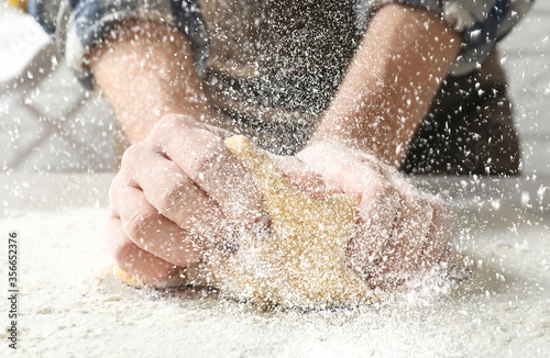 Young man kneading dough at table in kitchen  closeup