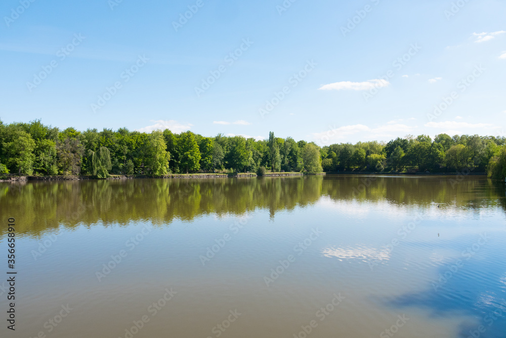 Beautiful lake during the spring season, Flers, Normandy, France. Green foliage in the background that reflects in the water. Sunny day in the park.