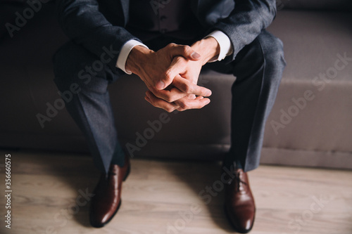 Men's fashion. The guy in the suit sits on the couch and folded his hands together.