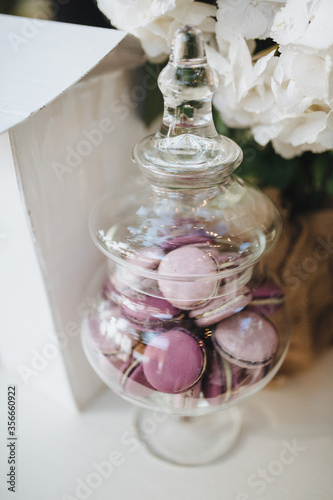 On a white wooden table is a glass vase with a sweet macaroon inside