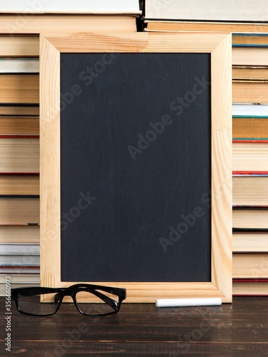 Chalk black board, glasses and chalk, against the background of books, copy space.