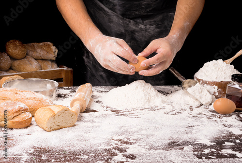 The table is full of flour and equipment for making bread and the chef is preparing the dough. On a black background