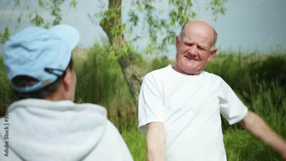 portrait of an old cheerful man performing physical exercises taking care of his health together with his wife during morning exercise in the park portrait of an old cheerful man performing physical exercises taking care of his health together with his wife during morning exercise in the park