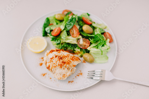 Bright fresh salad with greens, cherry and olives with chicken, sprinkled with paprika, slice of lemon and a fork on the white plate. 