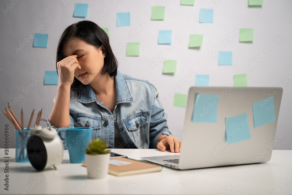 Asian woman working on a laptop tired and has eye pain sitting at home office. WFH. Work from home. Prevention Coronavirus COVID-19 concept. Asian woman working on a laptop tired and has eye pain sitting at home office. WFH. Work from home. Prevention Coronavirus COVID-19 concept.