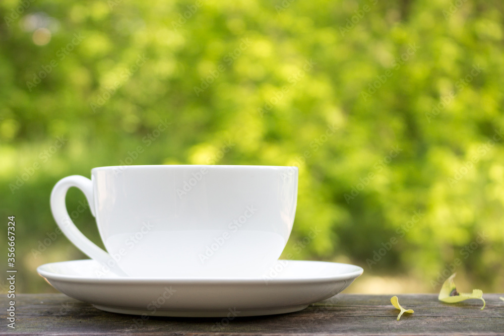 A white Cup on a wooden table on a Sunny summer day. An idyllic picture of the beginning of the day. Morning of a good day.