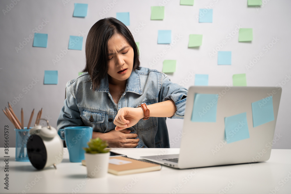 Asian woman working on a laptop was sick with stomach ache sitting at home office. WFH. Work from home. Prevention Coronavirus COVID-19 concept.
