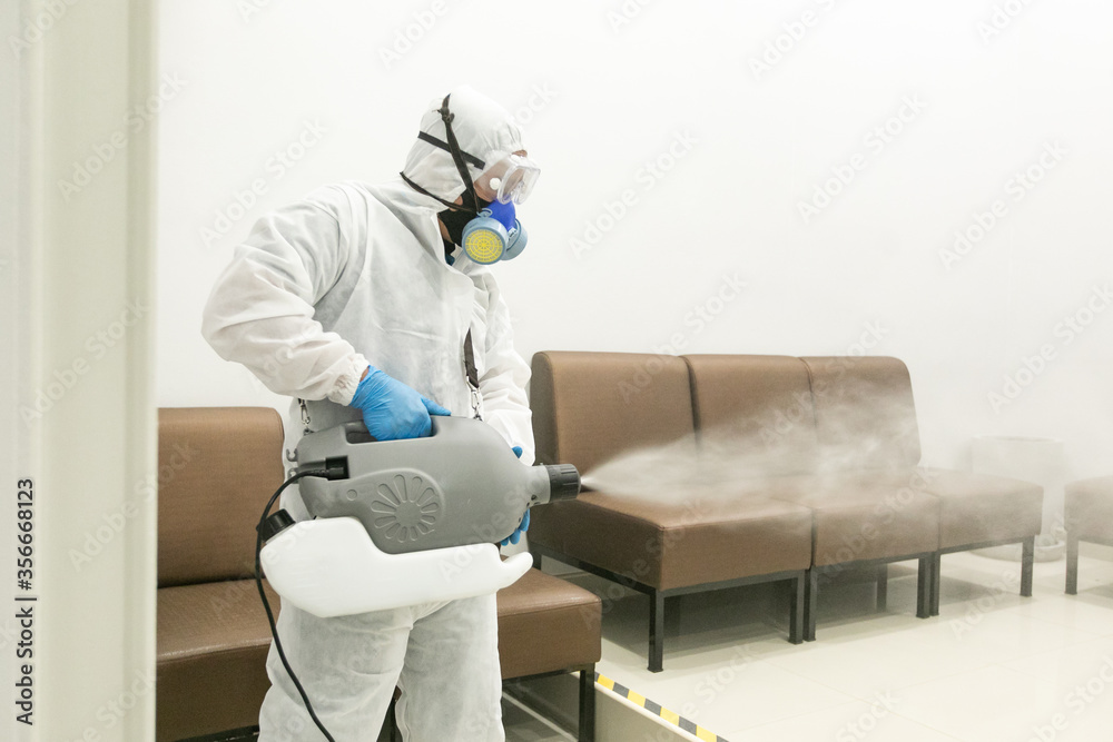 Worker wearing (ppe) protective equipment suit, gloves, mask, and chemical mask cleaning the room with machine of pressurized spray disinfectant water to remove covid-19 coronavirus. - obrazy, fototapety, plakaty 