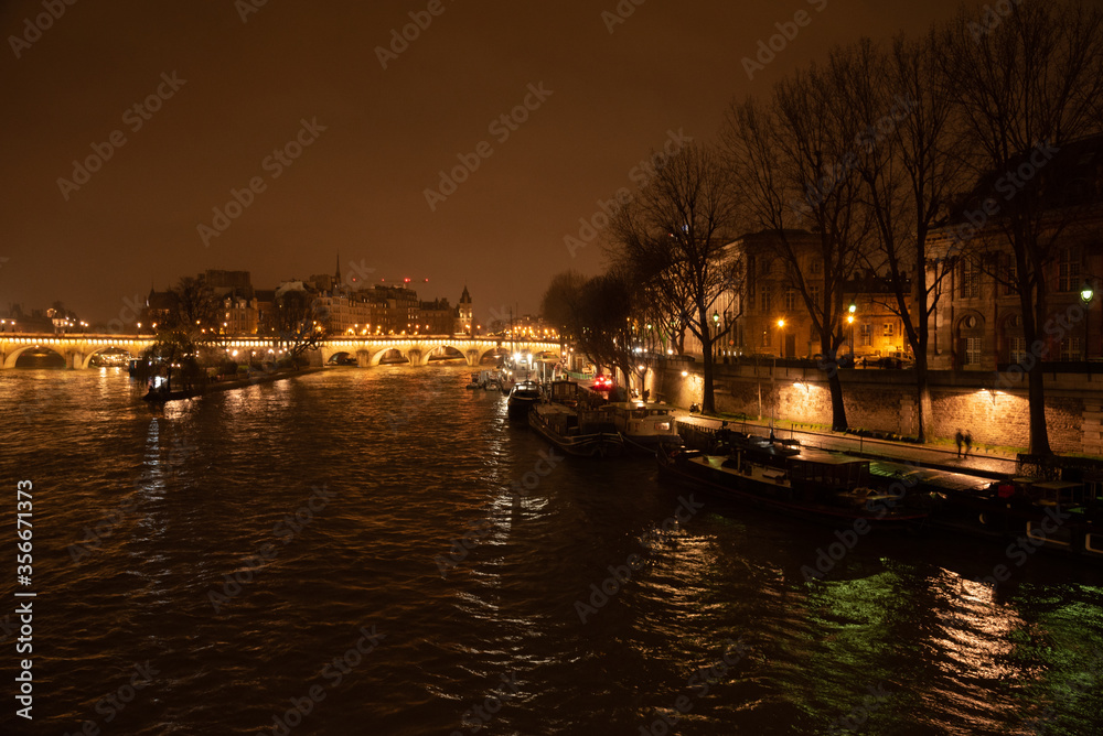 Paris, France. Night view of Seine river with boats, illuminated embankment and Pont Neuf (oldest standing bridge in city), people silhouettes, Ile de la Cite, reflections. Cityscape background.