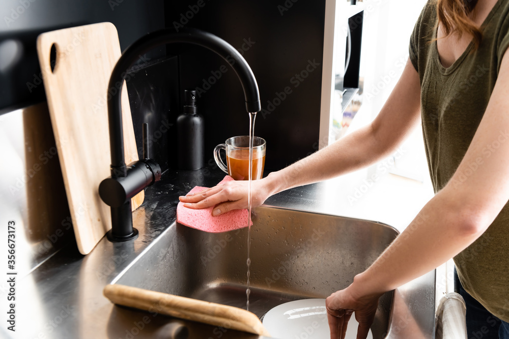 Cropped view of woman cleaning kitchen sink with rag