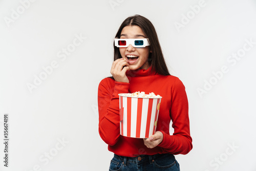 Photo of brunette woman wearing 3D glasses holding popcorn bucket