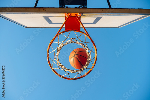 Street basketball ball falling into the hoop. Urban youth game. Close up of orange ball above the hoop net. Concept of success, scoring points and winning