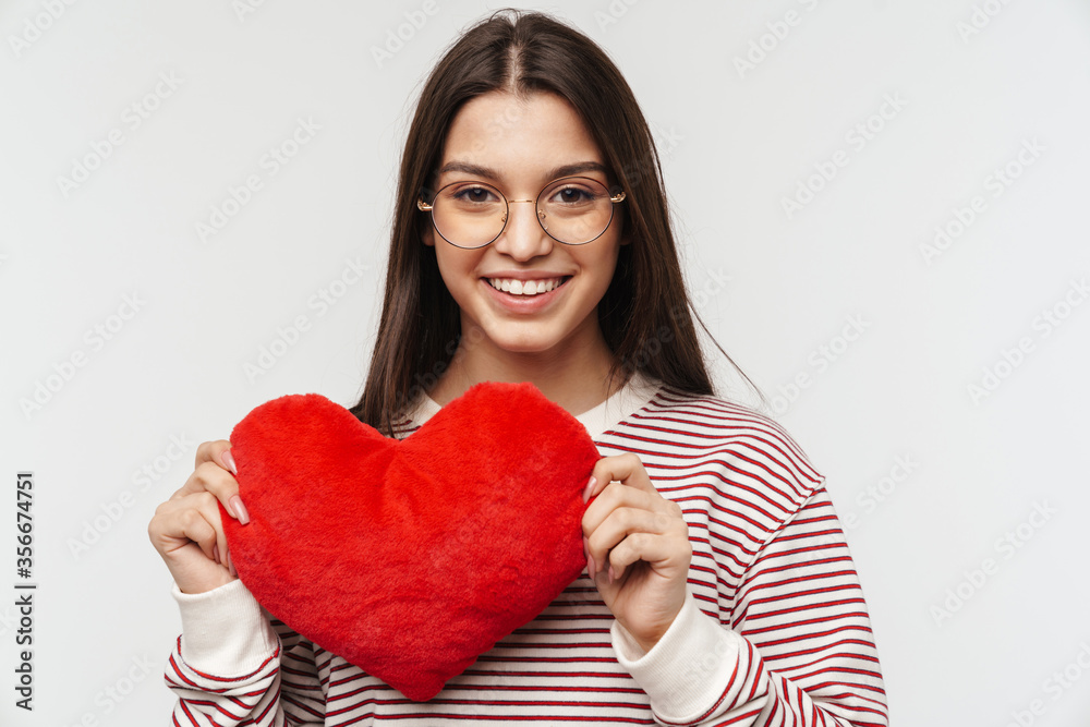 Photo of happy young woman smiling and holding heart shaped pillow Photo of happy young woman smiling and holding heart shaped pillow