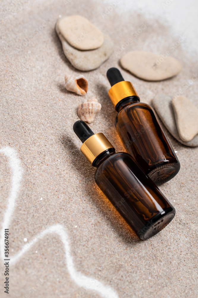 Glass brown bottles of serum with a pipette for skin care is on the sand with stones and shells. Cosmetics with marine components. The concept of health and beauty. minimalism