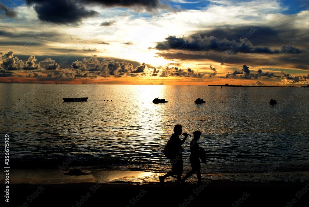 Beautiful sunset reflected in the waters of the Tinian, Northern Mariana Islands, with silhouettes of two people walking in the seashore.