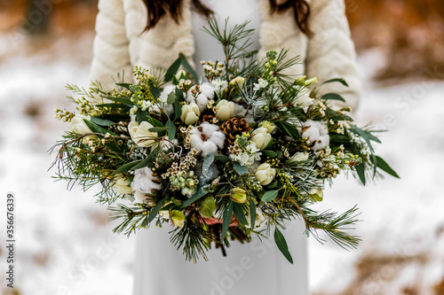 Bride holding a white wedding bouquet during a wedding ceremony in winter on snow in the middle of a forest covered with fresh snow