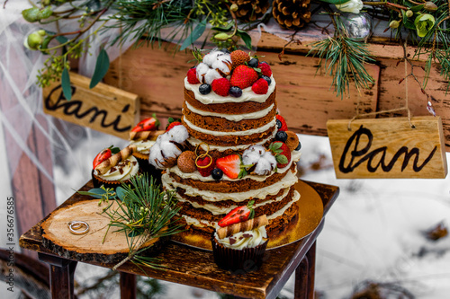 Wedding cake with fruit and an old wooden table with decorations and rings during a wedding ceremony in winter on snow in the middle of a forest covered with fresh snow
