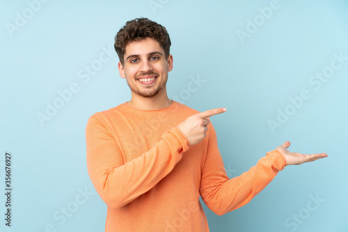 Caucasian man isolated on blue background holding copyspace imaginary on the palm to insert an ad