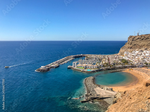 View from the air on the coast and bay in the city of Mogan on the Canary Islands where the bay harbor and people walking along the waterfront inside city
