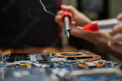 Close-up hand technician repairing broken laptop notebook computer with electric soldering Iron