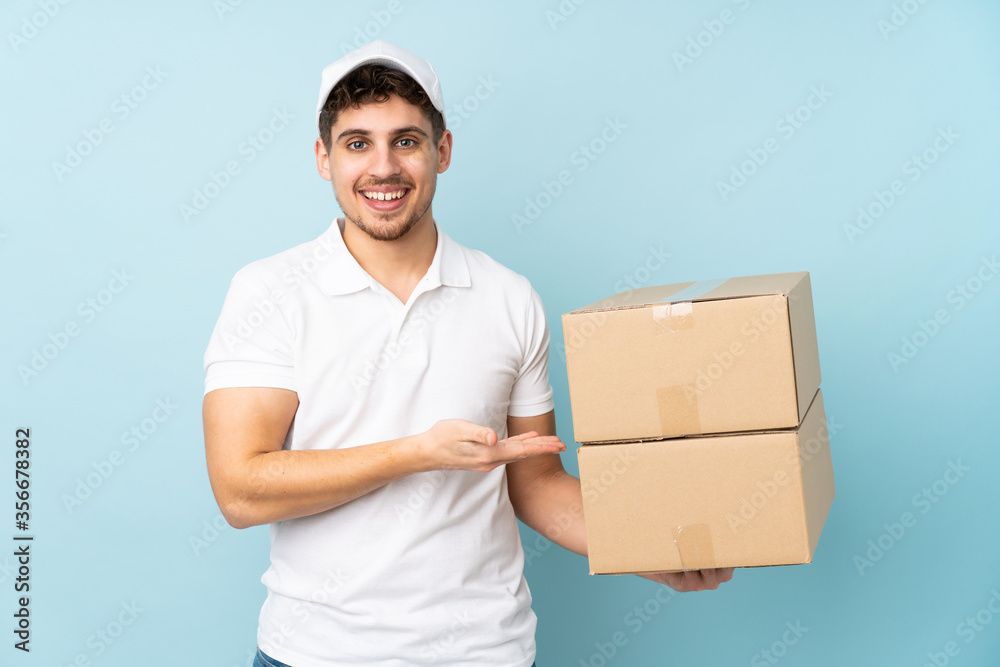 Delivery caucasian man isolated on blue background extending hands to the side for inviting to come Delivery caucasian man isolated on blue background extending hands to the side for inviting to come