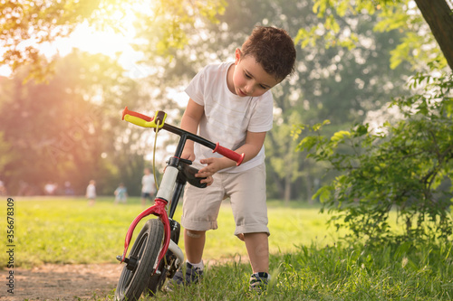 A little boy plays with his bicycle outside in the park on a sunny day.