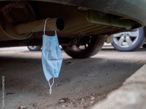 Canvas Print A medical mask hangs on the exhaust pipe of a car