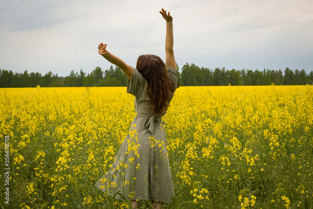 Young woman in sleeveless dress enjoying sunlight and nature on yellow blooming rapeseed field Young woman in sleeveless dress enjoying sunlight and nature on yellow blooming rapeseed field