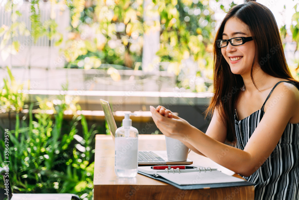 Young 20s Asian beautiful woman with attractive smile using hand sanitizer gel to wash her hands. While using computer laptop and mobile phone outside in cafe scene. - Corona Virus prevention concept. Young 20s Asian beautiful woman with attractive smile using hand sanitizer gel to wash her hands. While using computer laptop and mobile phone outside in cafe scene. - Corona Virus prevention concept.