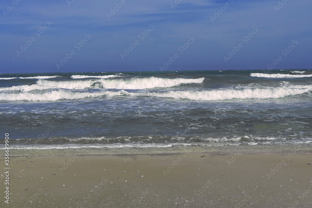 Wet sand, a sea with dark-colored waves and a deep blue sky