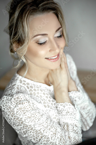 Female portrait of beautiful wedding make-up and hairstyle. The face of woman is posing with close eyes to show mua. The morning of bride dressed white openwork dress