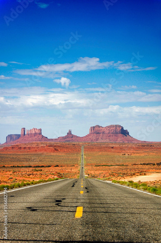 Highway in the desert vanishing towards the sunstone buttes of Monument Valley.