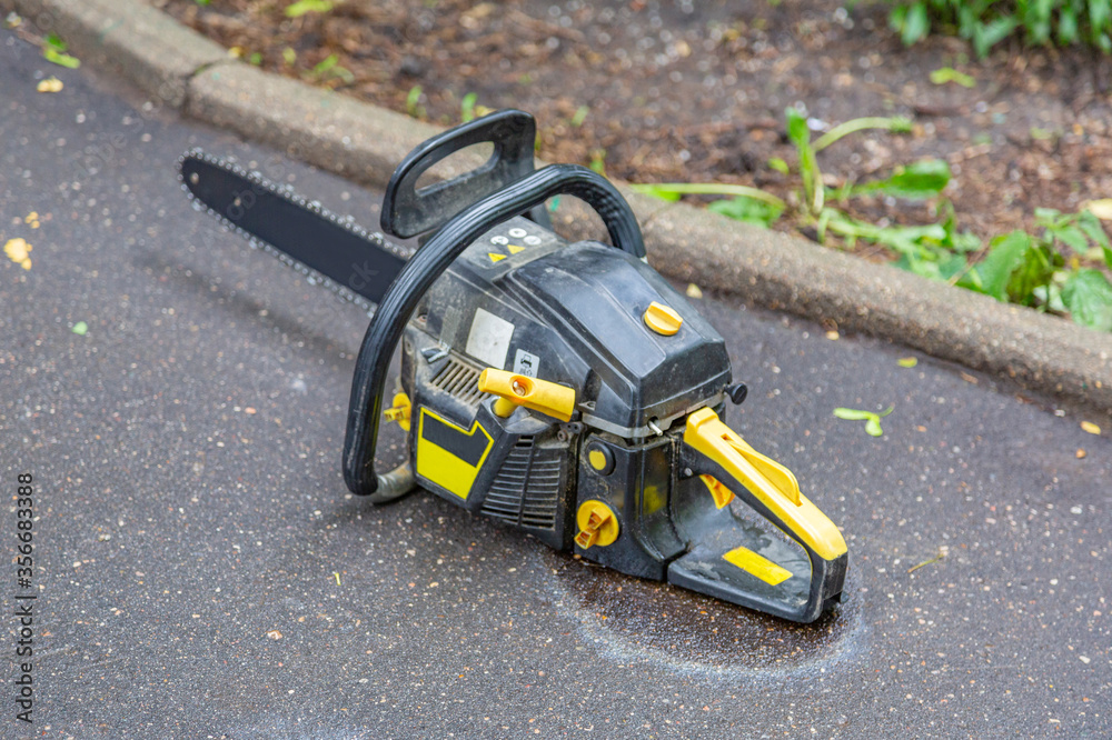 Fototapeta premium Powerful chainsaw for cutting wood lies on wet asphalt