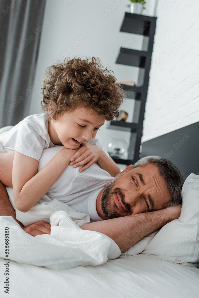 curly boy looking at bearded father lying on bed curly boy looking at bearded father lying on bed