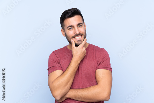 Young handsome man with beard over isolated blue background smiling