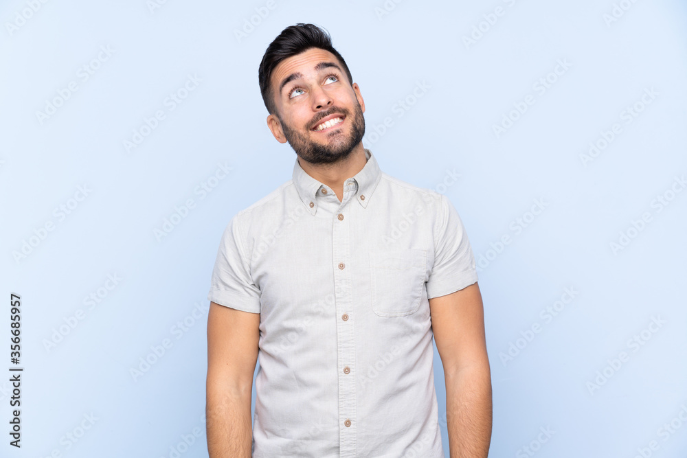 Young handsome man with beard over isolated blue background laughing and looking up Young handsome man with beard over isolated blue background laughing and looking up