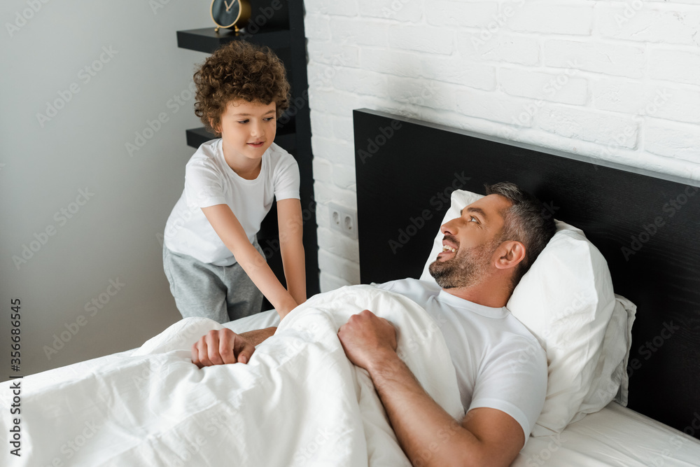 Fototapeta premium curly kid touching happy father lying in bed