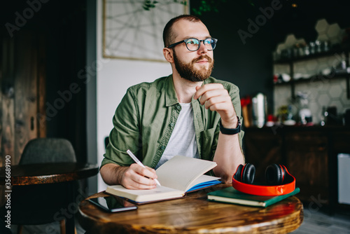 Handsome creative author sitting at cafe interior with notebook photo