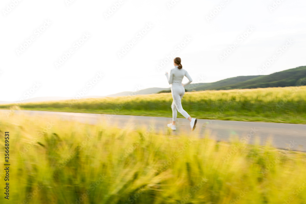 Sportliche junge Frau joggt abends zwischen Feldern