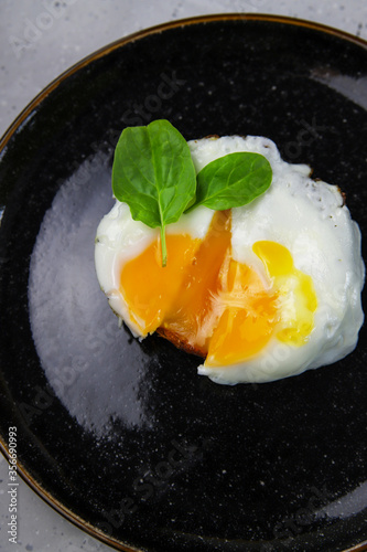 Fried egg toast with fresh baby spinach on black plate on gray concrete background. Tasty healthy breakfast. Morning food, top veiw
 photo