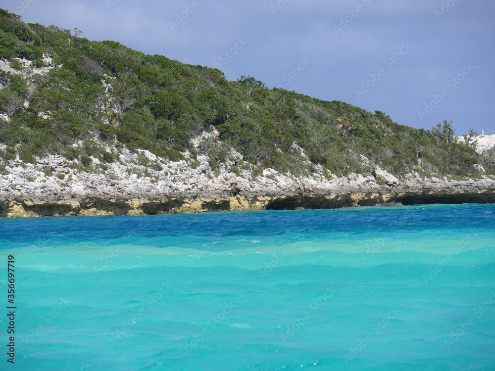 Rocky island covered in  lush greens with the different hues of blue waters of Exuma Cays, Bahamas. The islands are a popular destination for tourists.