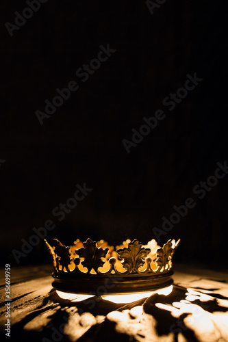 Vertical photo for posters and banners. A crown on a black background is highlighted with a golden beam. One to one. Low-key image of a beautiful queen . Fantasy of the medieval period. Game. Thrones.