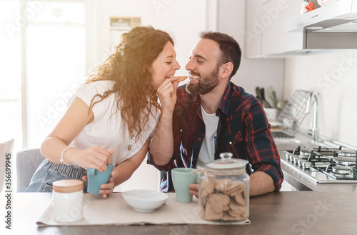 Engaged couple has breakfast together in their new home - young couple jokes while eating cookies - love and well-being concept - warm filter on background.