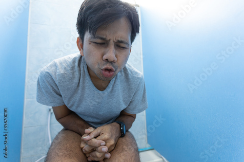 young asian man has a stomach ache sitting on a toilet bowl in the bathroom. Diarrhea