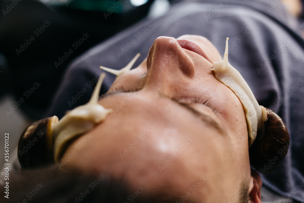 Naklejka premium Caucasian young man receiving snails massage. Face skin therapy and care with snails in spa salon. Modern cosmetological procedure of skin rejuvenation.