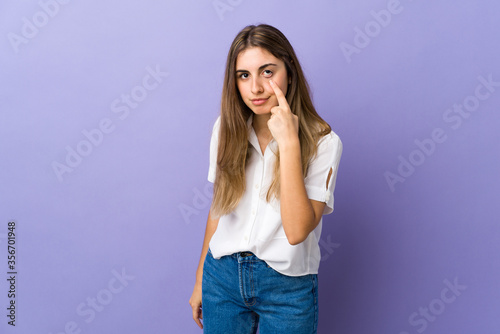 Young woman over isolated purple background showing something